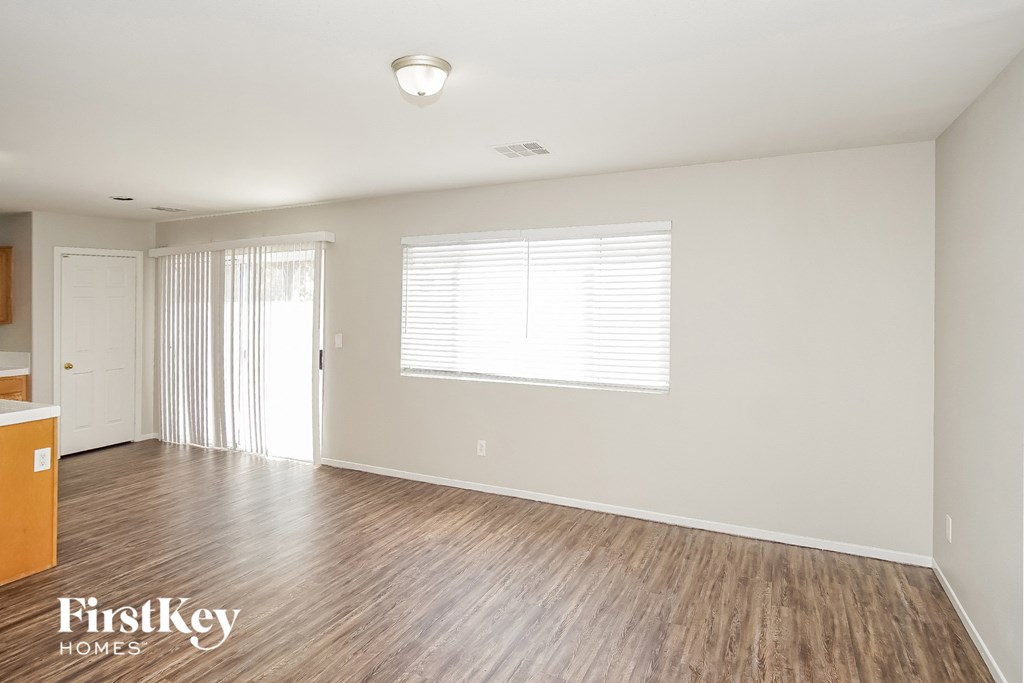 A spacious room with wooden flooring and a window with blinds.