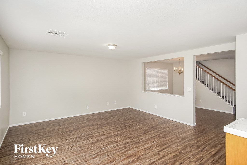 A spacious room with wooden flooring and a staircase on the right.