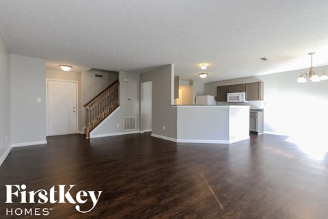A spacious living room with wood flooring and a kitchen in the background.
