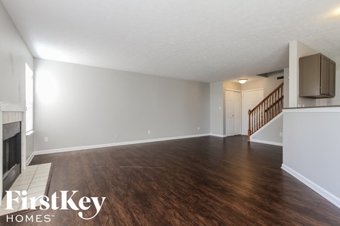 A spacious room with wooden flooring and a staircase in the background.