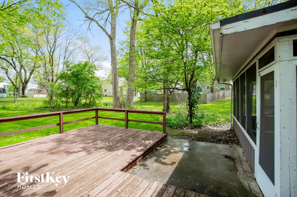 a deck overlooking a yard with trees and a house