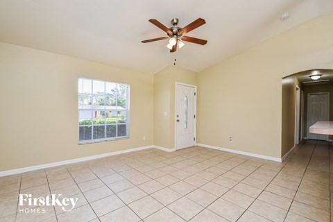A spacious room with a ceiling fan and a window overlooking a fence.