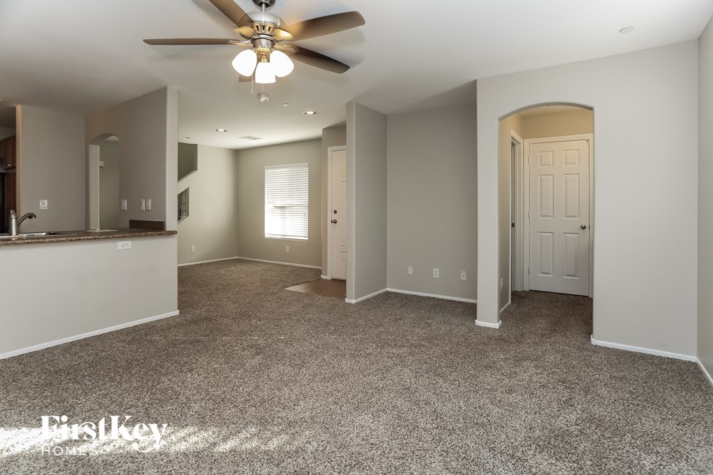 an empty living room with a ceiling fan and a kitchen