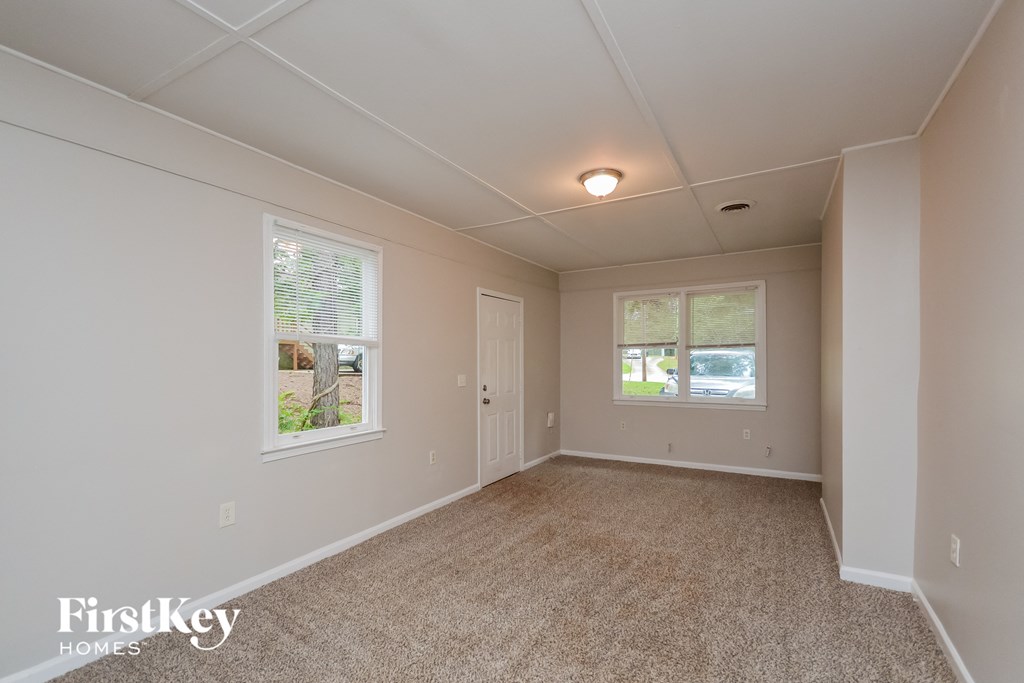 A spacious room with a carpeted floor and two windows.