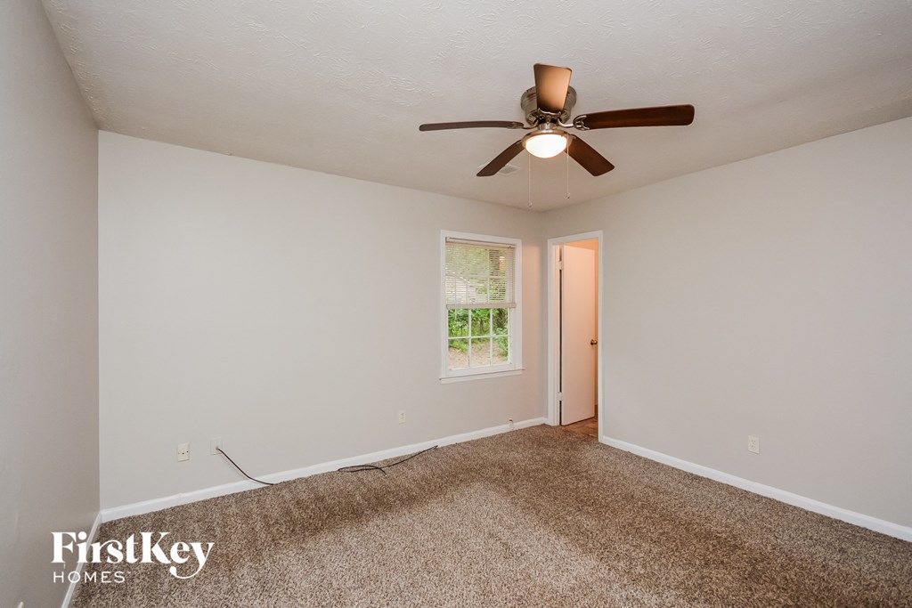 A room with a ceiling fan and a window with a view of trees.