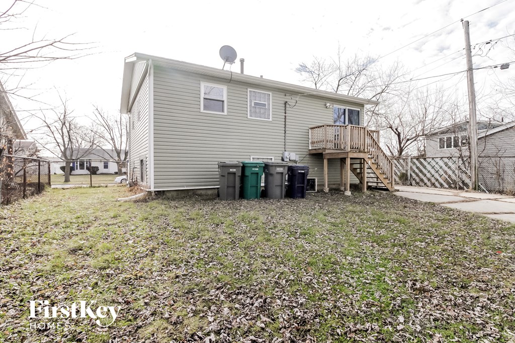 A small house with a grey roof and a balcony is surrounded by a grassy area with a FirstKey HOME sign.