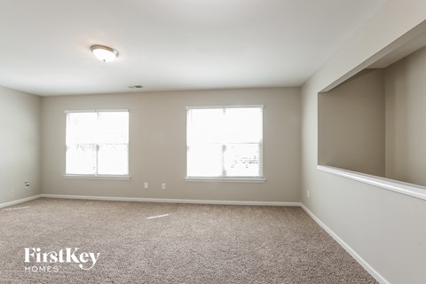 A sparsely furnished room with a carpeted floor and two windows.