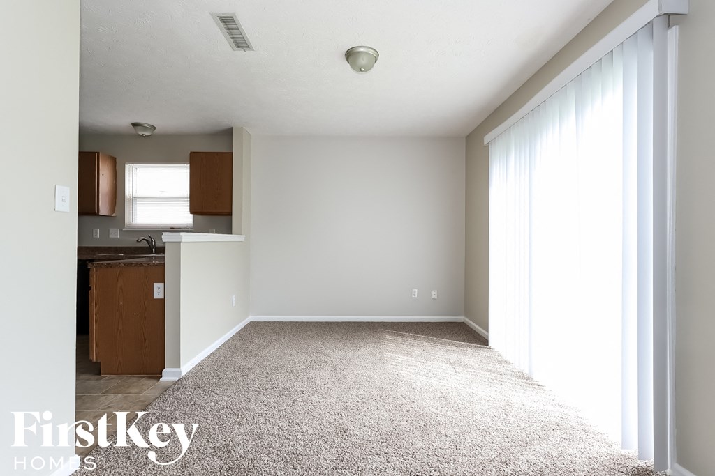 an empty living room with white carpet and a kitchen