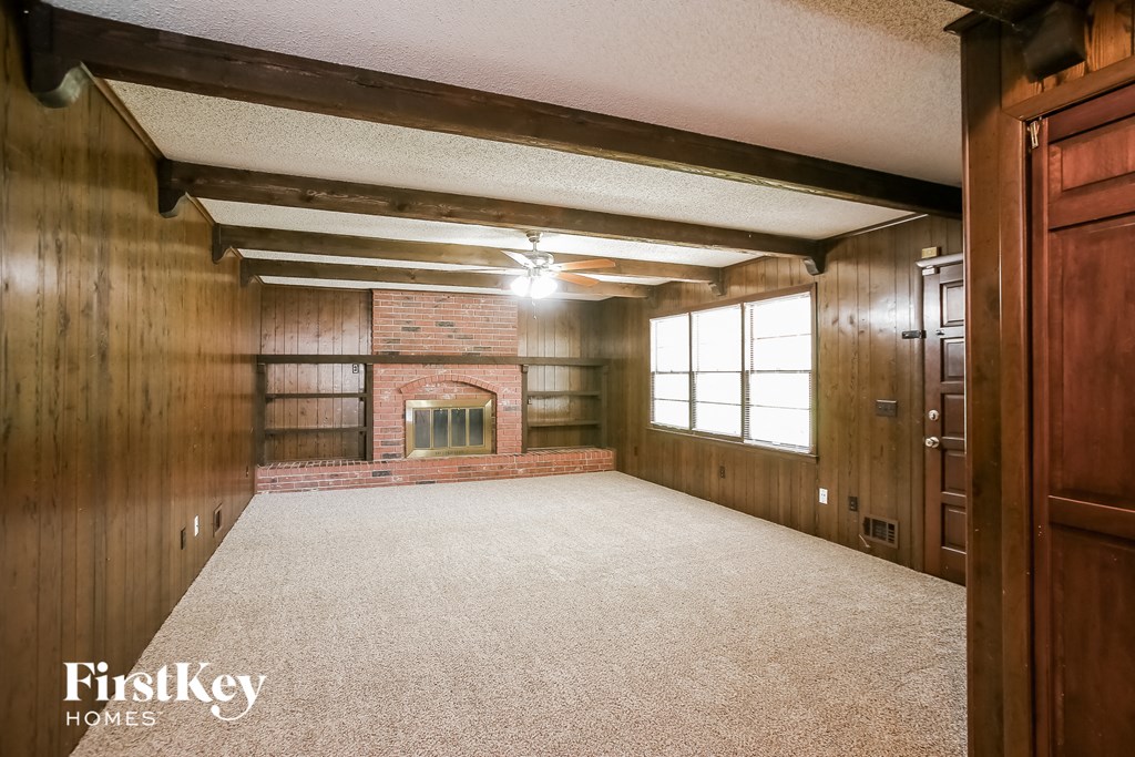 an empty living room with a brick fireplace and wood paneling