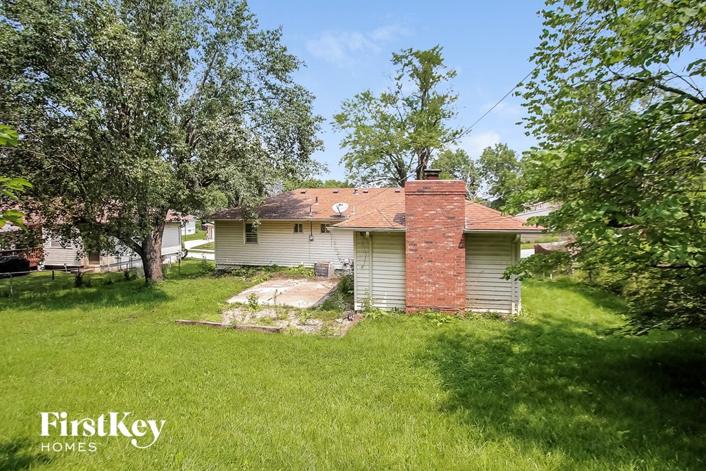 a small white house with a red brick chimney in the yard