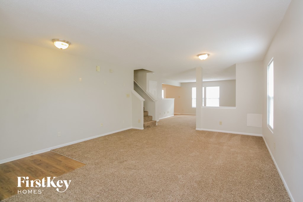 a spacious living room with white walls and carpeting and a staircase