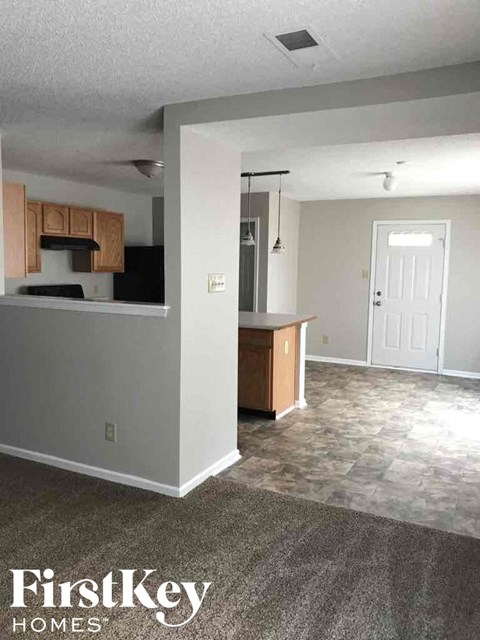 A kitchen area with a counter and cabinets is shown in a room with a carpeted floor.