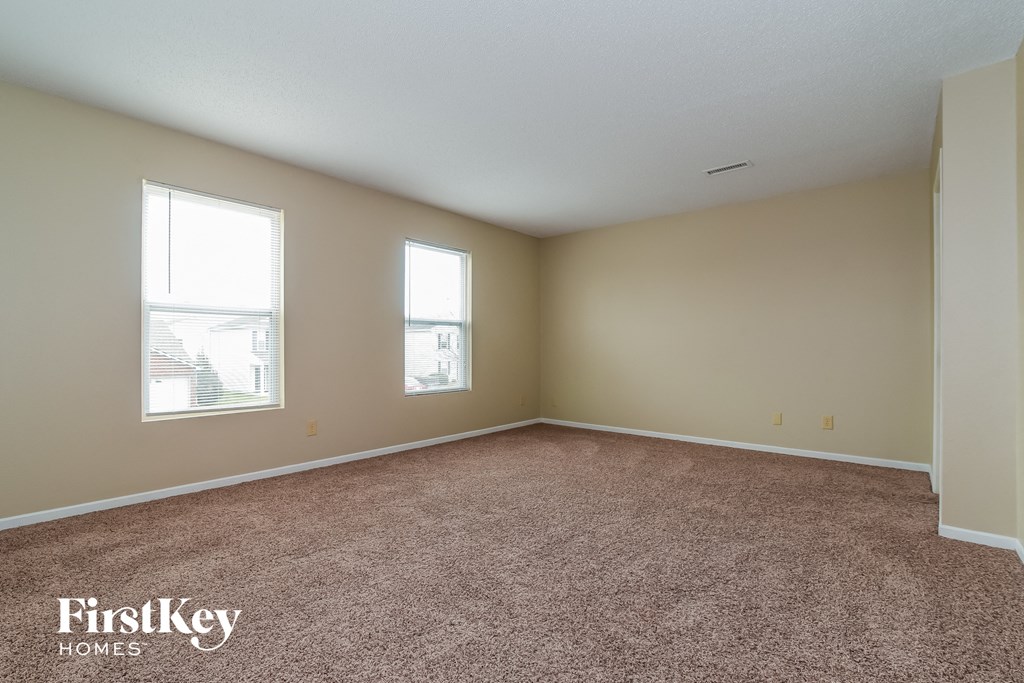 an empty living room with carpet and two windows