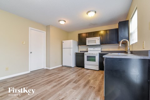 a kitchen with black cabinets and white appliances and wood flooring