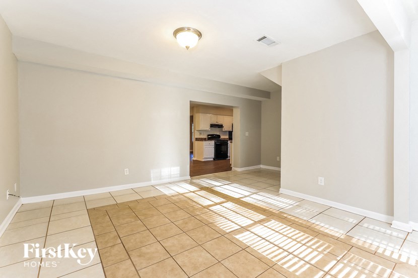 an empty living room with tiled floors and a kitchen in the background