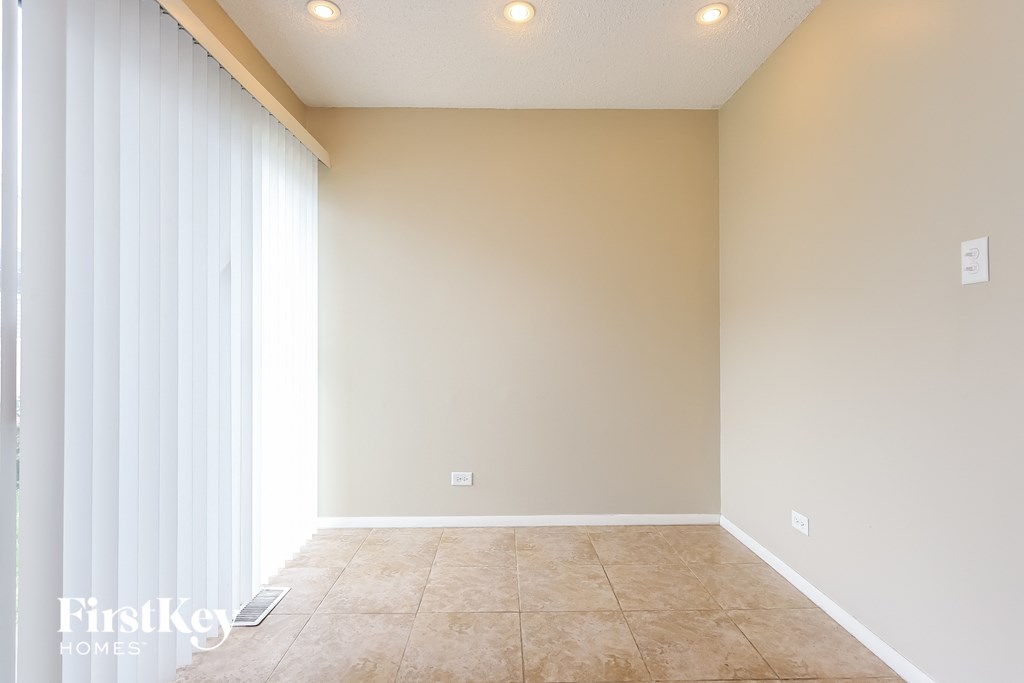 A room with beige walls and floor, a window with white blinds, and recessed lighting.