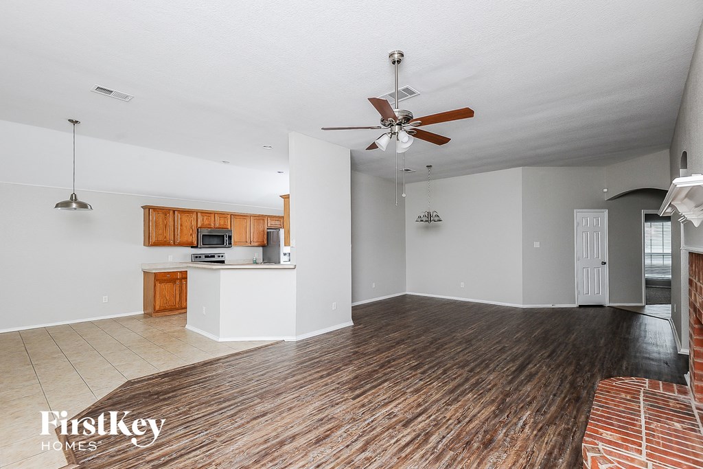 an empty living room with a ceiling fan and a kitchen