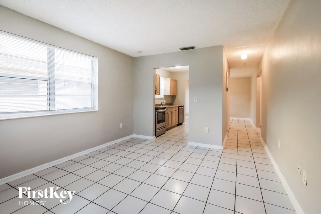an empty living room with a tiled floor and a kitchen