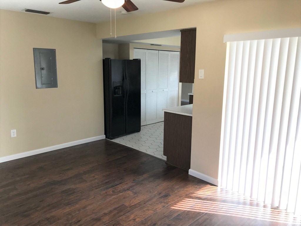 A room with a black fridge and wooden floors.