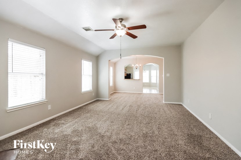 a carpeted living room with a ceiling fan and a window
