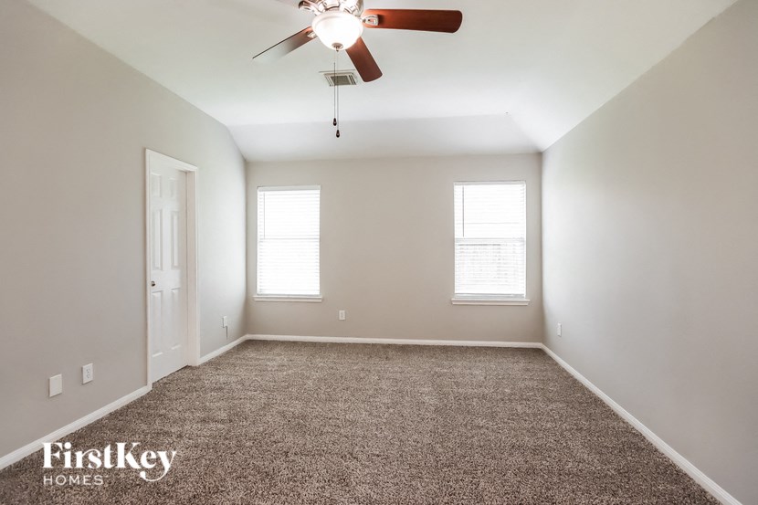 a carpeted room with a ceiling fan and two windows