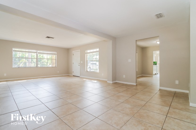 an empty living room with tiled flooring and a door to the kitchen
