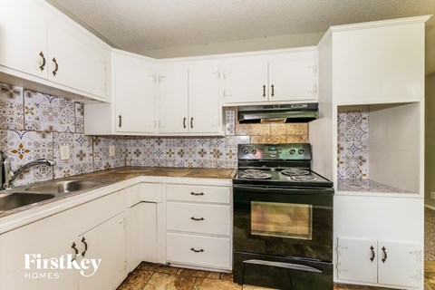 A kitchen with a black stove top oven and white cabinets.