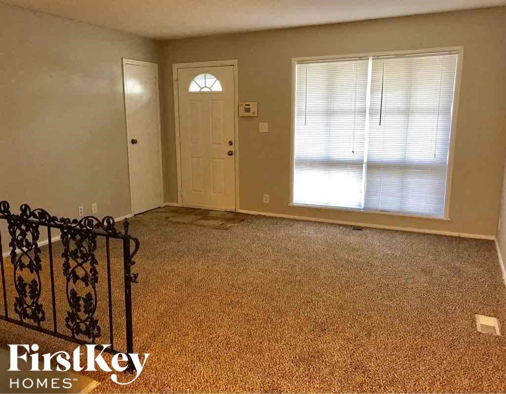 A room with a carpeted floor, a door, and a window with blinds.