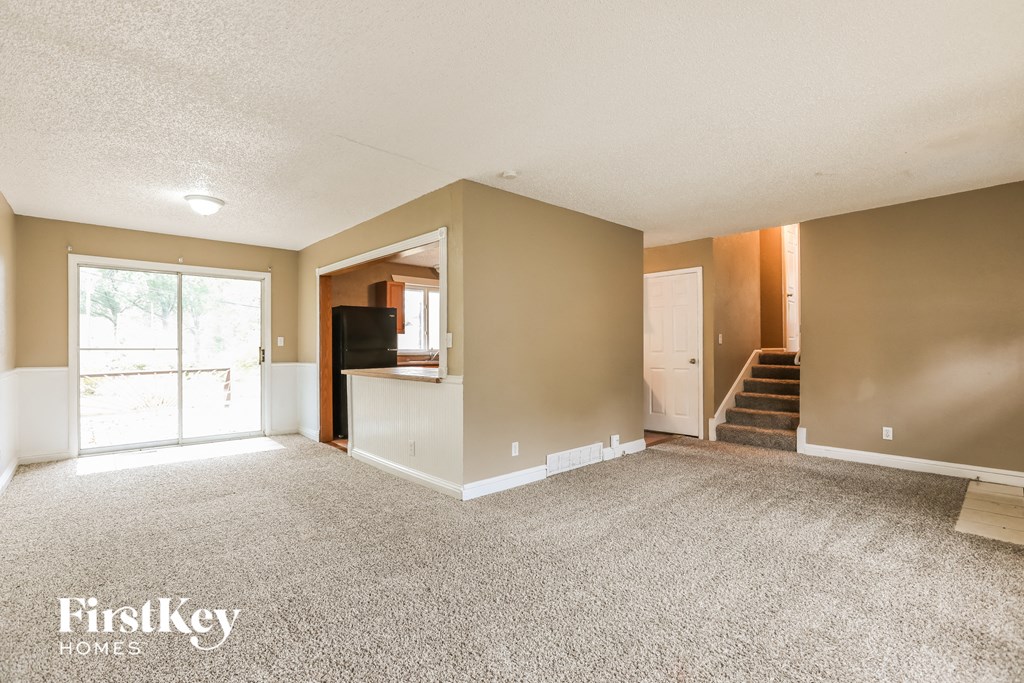an empty living room with carpet and a door to a staircase