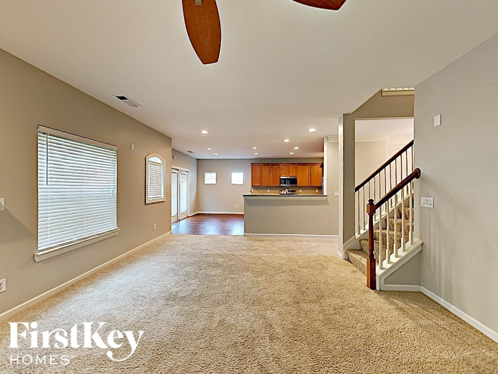 an empty living room with a staircase and a kitchen