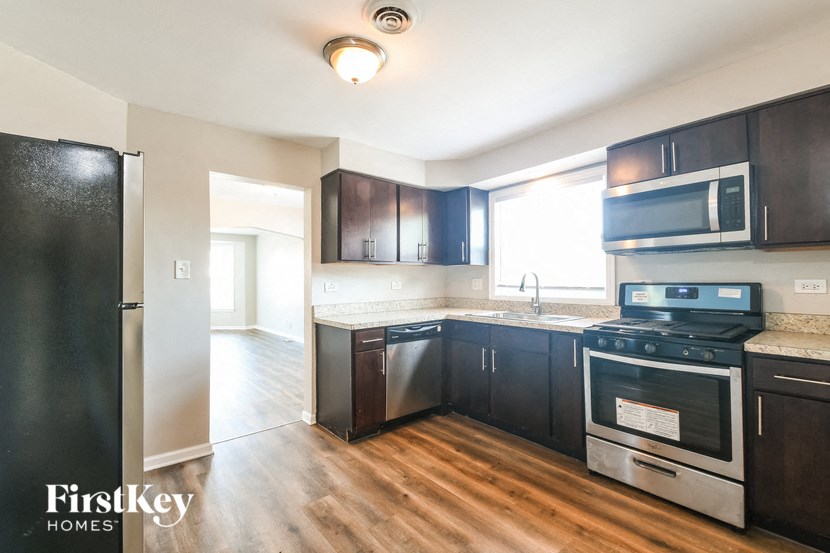 an empty kitchen with black cabinets and stainless steel appliances and wood flooring