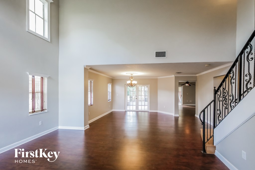 A spacious living room with wood floors and a staircase with black railings.