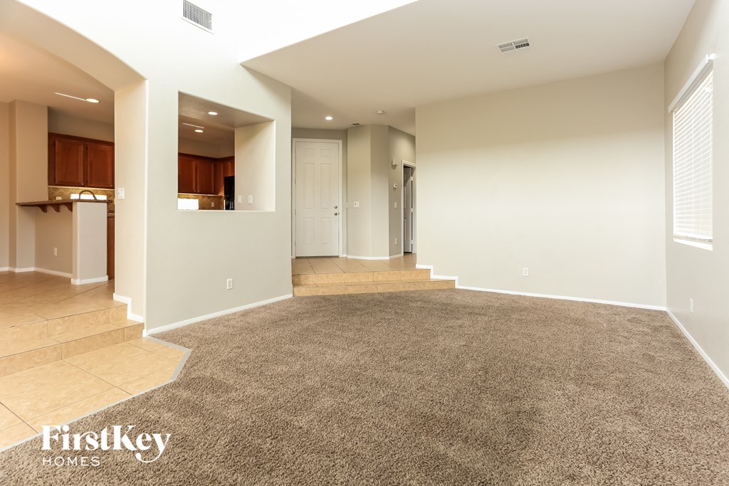 A spacious living room with a carpeted floor and a staircase leading to the upper level.