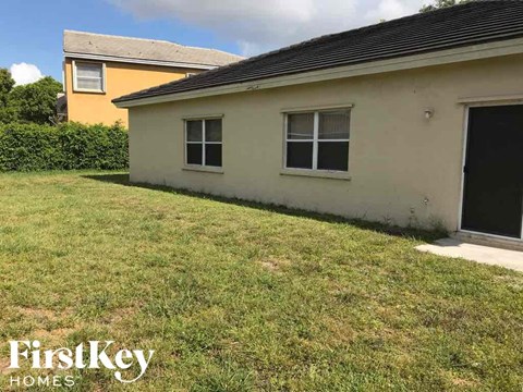 A small house with a black door and two windows is surrounded by a grassy area.