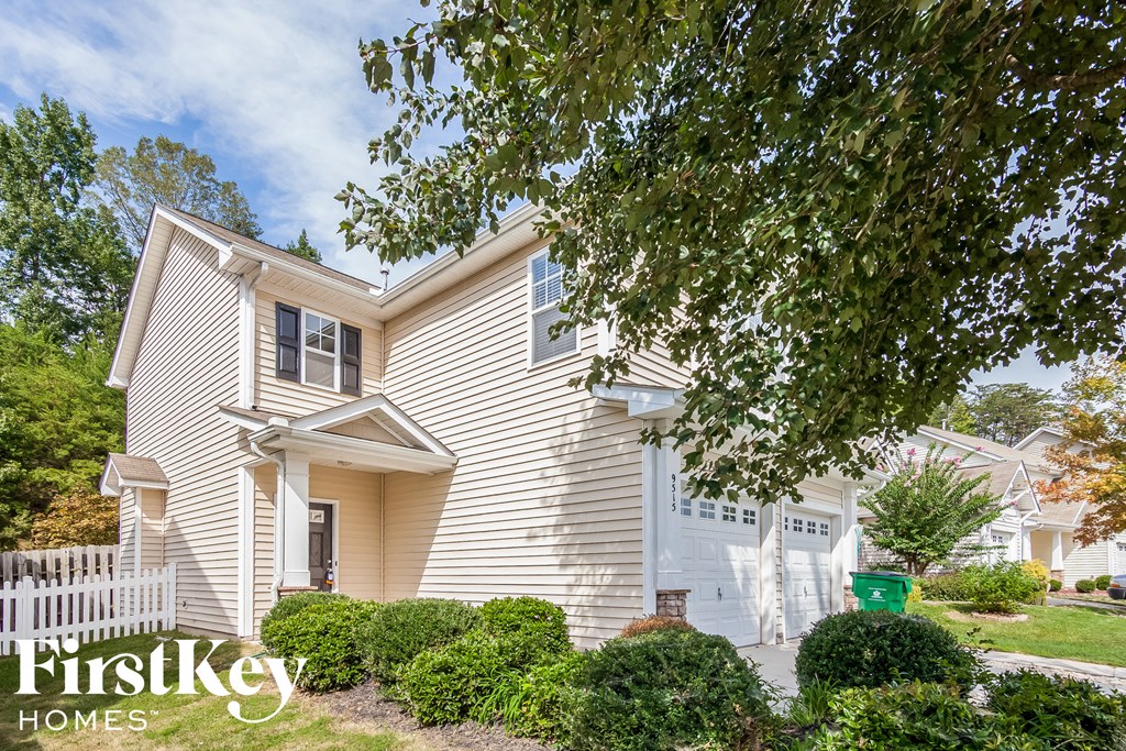 A house with a white picket fence and a tree in front of it.