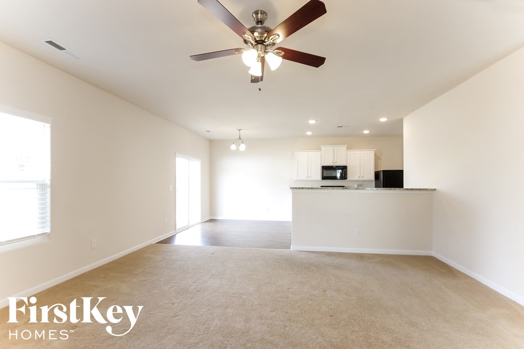 A spacious, empty room with a ceiling fan and a flat screen TV mounted on the wall.