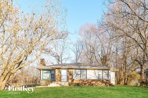 a small bungalow on a lawn with trees