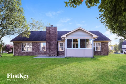 A house with a brick chimney and a white door is surrounded by a grassy lawn.