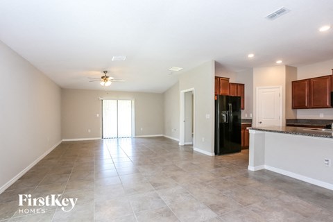 A spacious kitchen and living room with a black refrigerator and wooden cabinets.