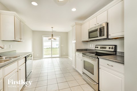A kitchen with white cabinets and appliances, a chandelier, and a large window.