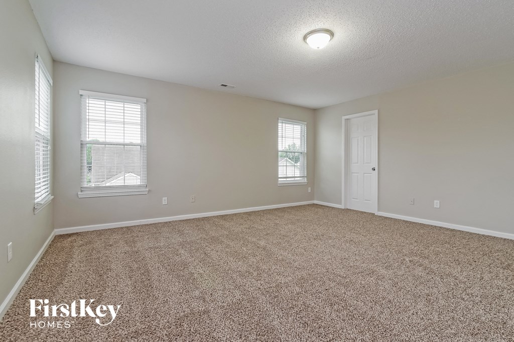 a spacious living room with carpet and two windows