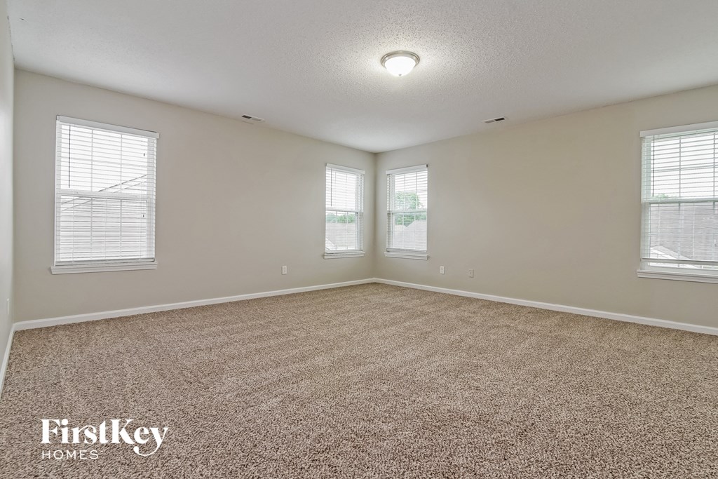 the living room of an empty house with carpet and three windows