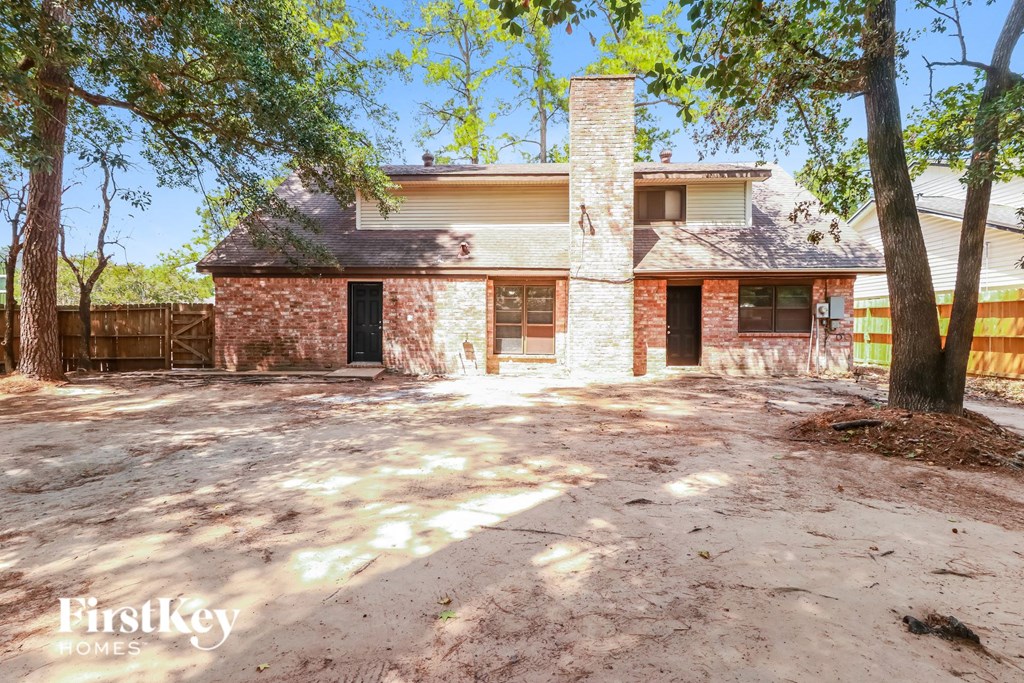 a brick house with a dirt driveway and trees