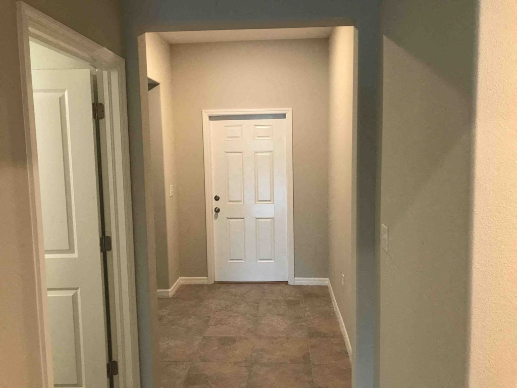 a room with a white door and a hallway with a tile floor and a closet
