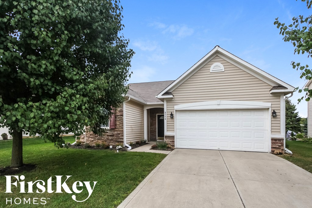A house with a garage door and a tree in front of it.