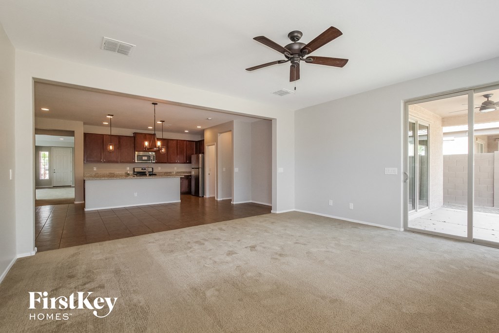 an empty living room with a ceiling fan and a kitchen