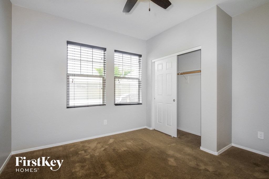a bedroom with a closet and two windows and a ceiling fan