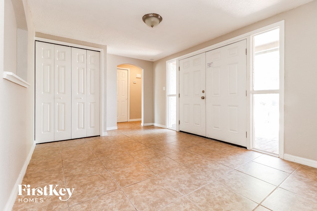 A spacious room with a tiled floor and white walls, with a door on the left and a window on the right.