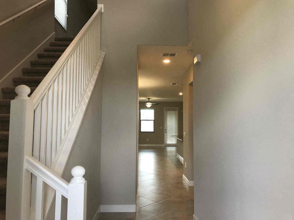 A hallway with a staircase on the left and a door on the right.