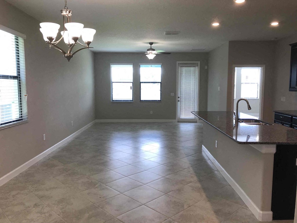A spacious kitchen and living room with tile flooring and a chandelier.